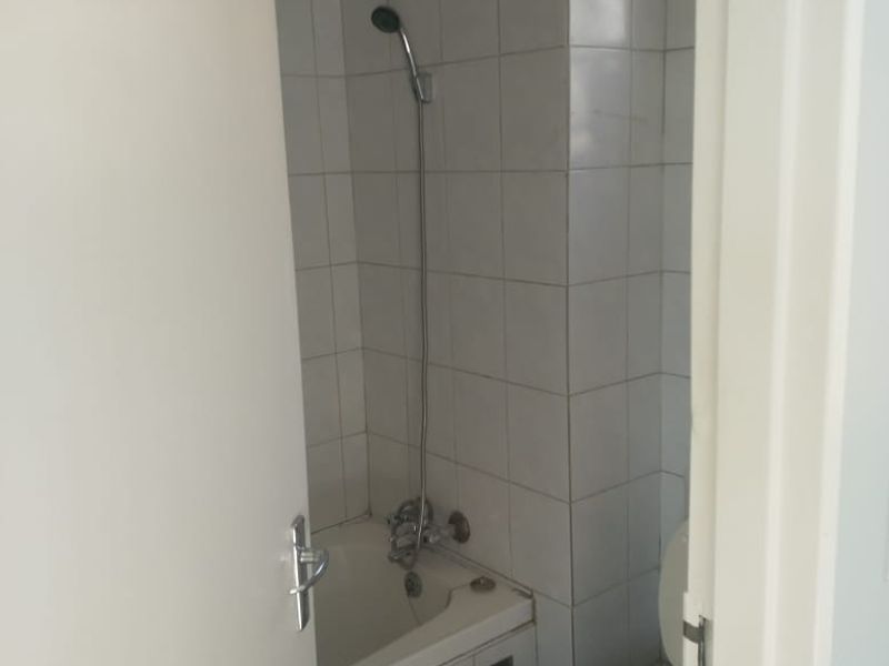 A compact bathroom featuring a built-in bathtub with shower mixer and a standard toilet, finished with white wall tiles.