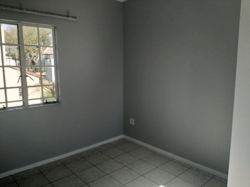 An empty bedroom featuring grey painted walls, tiled flooring, and a window with security bars.