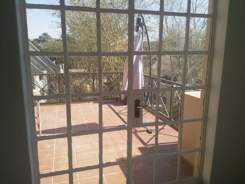 A view through french doors onto an outdoor balcony featuring tiled flooring and a metal safety balustrade.