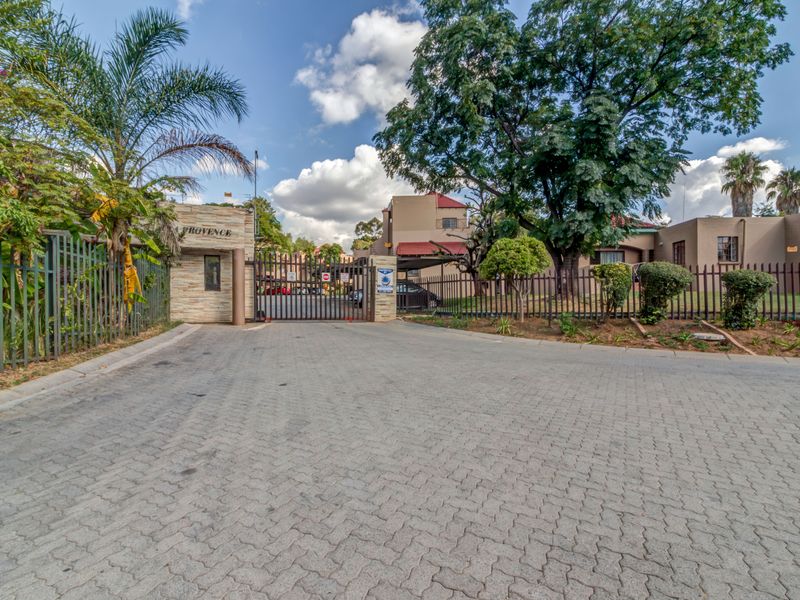 Front entrance view of the apartment complex featuring a secure gated access point, paved driveway, and perimeter fencing.