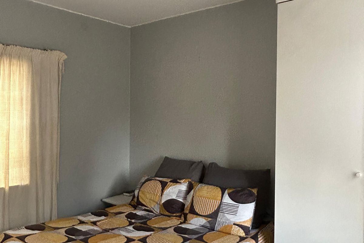 A functional bedroom featuring a built-in wardrobe, tiled flooring, and a ceiling-mounted spotlight fixture.