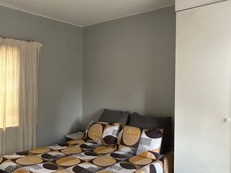 A functional bedroom featuring a built-in wardrobe, tiled flooring, and a ceiling-mounted spotlight fixture.