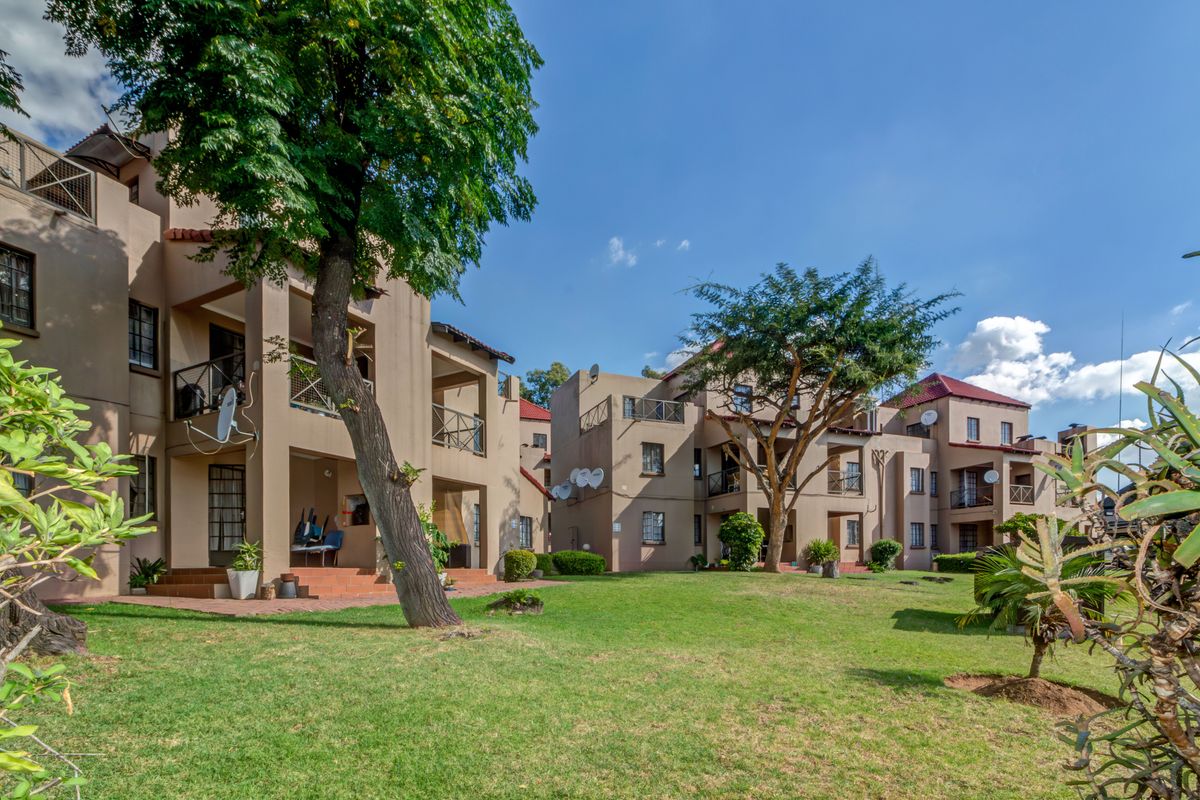 A view of the apartment complex rear facade featuring private balconies, ground floor patios, and well-maintained communal garden areas.