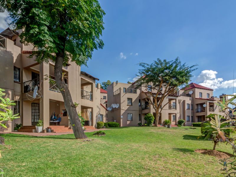 A view of the apartment complex rear facade featuring private balconies, ground floor patios, and well-maintained communal garden areas.