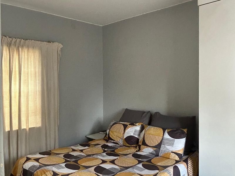 A functional bedroom featuring tiled flooring, a built-in wardrobe, and a ceiling-mounted spotlight fixture, offering a neutral base for personalization.