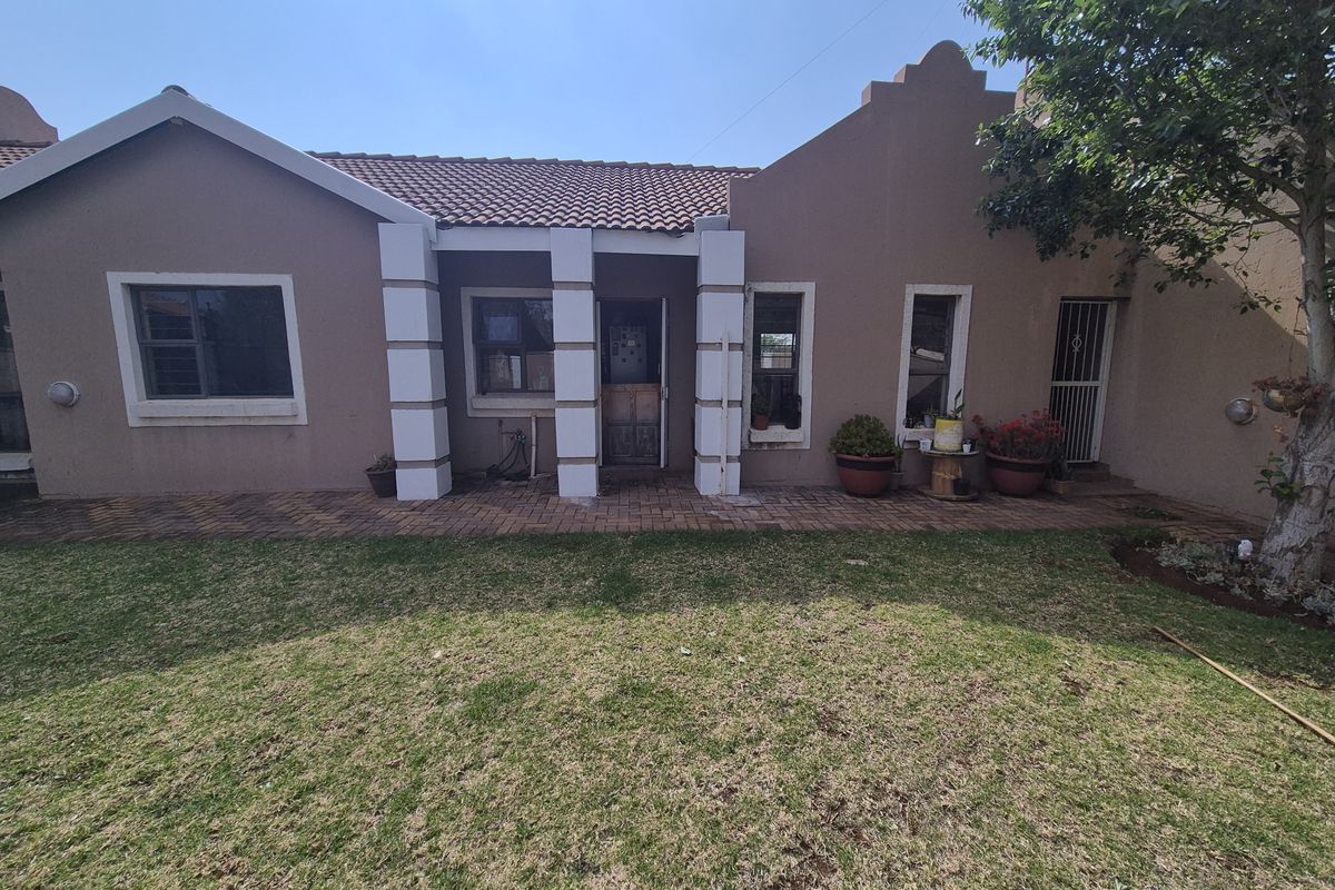 Rear view of the property featuring a plastered facade, tiled roof, and a brick-paved patio area overlooking the garden.