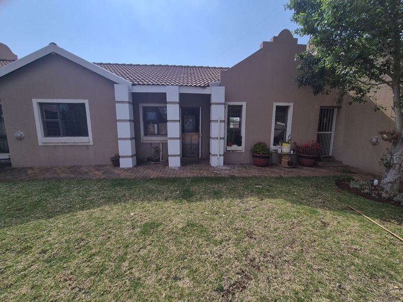 Rear view of the property featuring a plastered facade, tiled roof, and a brick-paved patio area overlooking the garden.