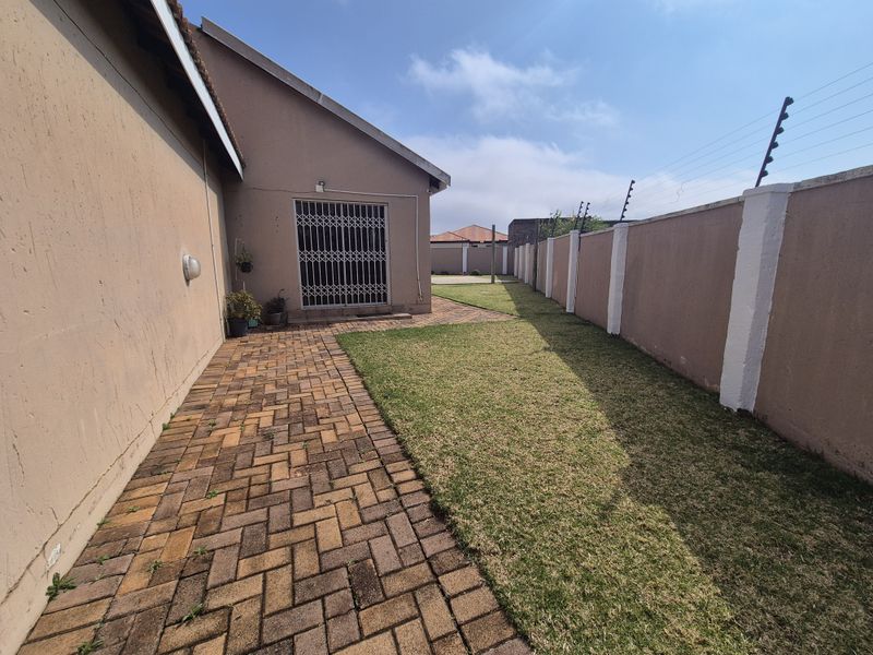 A private rear garden featuring a paved walkway, a well-maintained lawn, and secure perimeter walling with electric fencing.