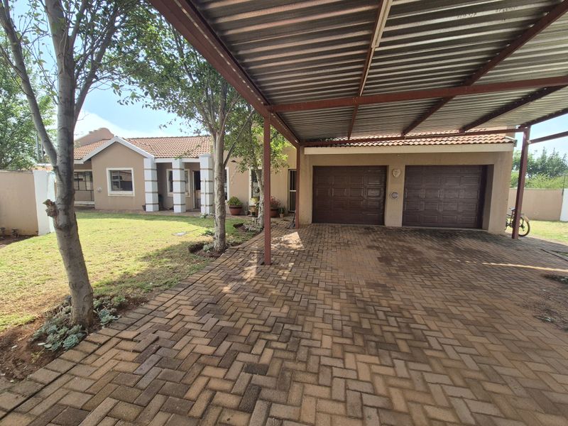 Front view of the property featuring a paved driveway, a covered carport, and a double garage with a well-maintained garden area.