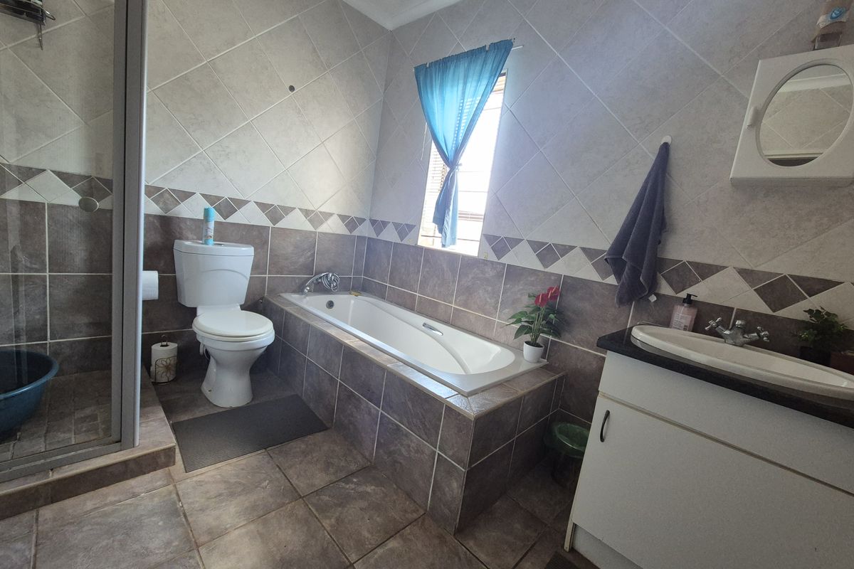 A functional bathroom featuring a built-in bathtub, separate shower enclosure, vanity basin, and tiled finishes throughout.