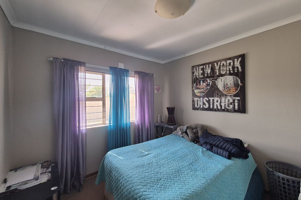 A standard bedroom featuring a window with security bars, neutral wall paint, and a central ceiling light fixture.