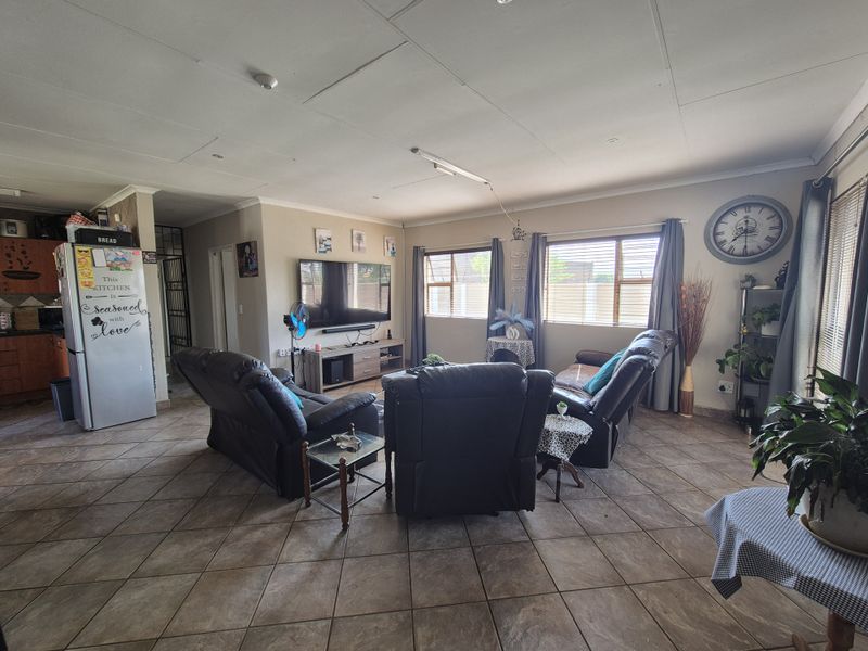 Spacious open-plan living area featuring tiled flooring and an integrated kitchen, offering a functional layout with ample natural light through large windows.