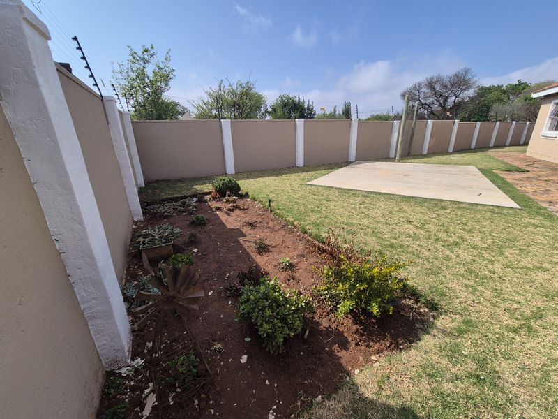A private rear garden featuring a perimeter wall with electric fencing, a concrete patio area, and established garden beds.