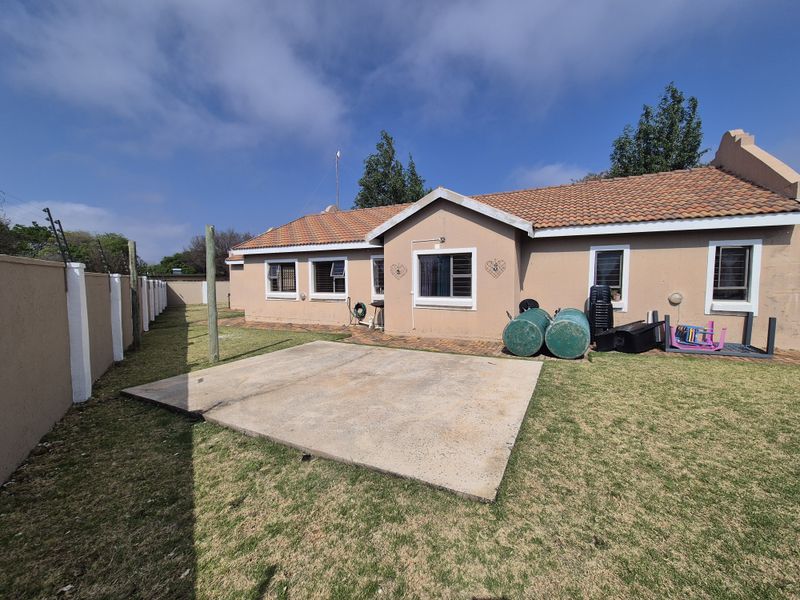 Rear view of the house featuring a concrete patio, lawn, and perimeter wall with electric fencing.