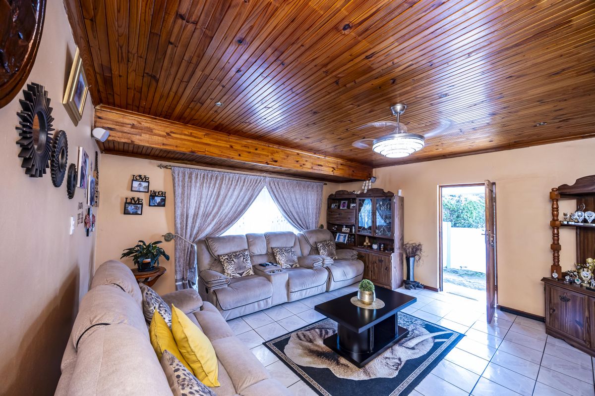 A living room featuring a warm timber tongue and groove ceiling with exposed beams, ceramic tiled flooring, and a ceiling fan.