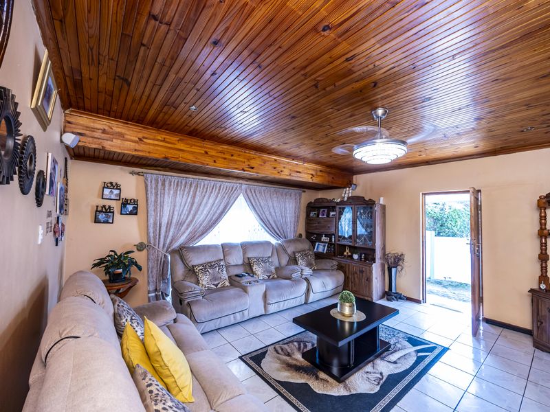 A living room featuring a warm timber tongue and groove ceiling with exposed beams, ceramic tiled flooring, and a ceiling fan.