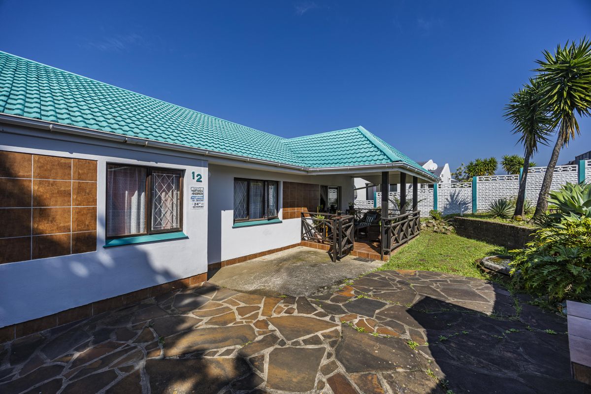 Rear exterior view of the property featuring a covered patio, stone paved area, and a tiled roof.