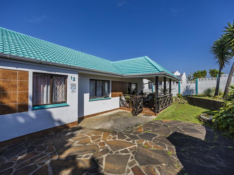 Rear exterior view of the property featuring a covered patio, stone paved area, and a tiled roof.