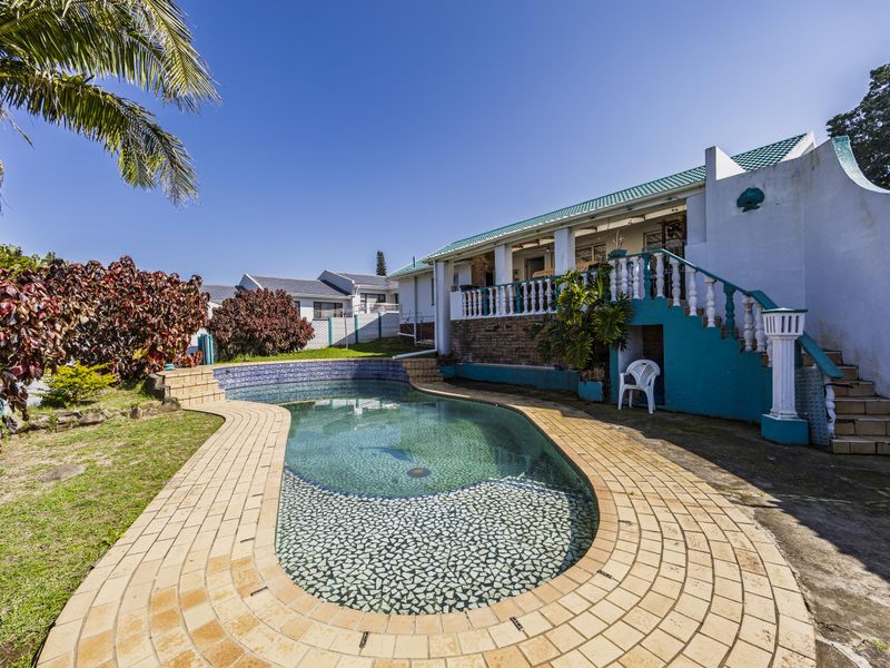 Outdoor pool area featuring a curved swimming pool with brick coping, adjacent to a raised patio with a concrete staircase and balustrade.