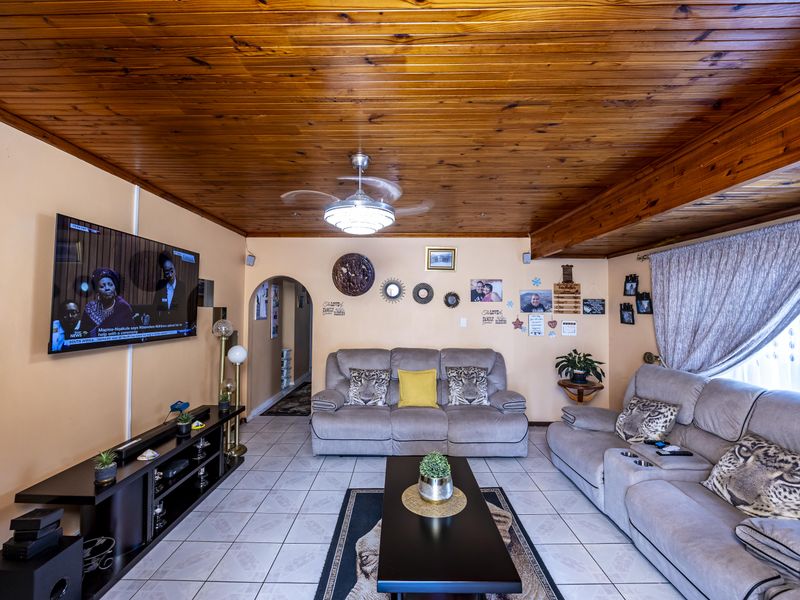A living room featuring a timber tongue and groove ceiling, ceiling fan, and ceramic floor tiles, with an arched entryway leading to other areas.