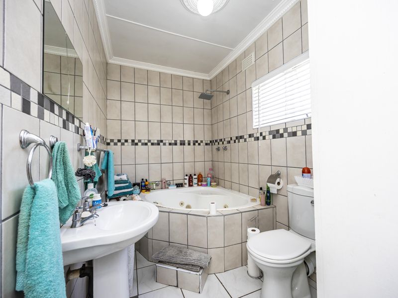 A functional bathroom featuring a corner jetted bathtub, wall-mounted shower, pedestal basin, and tiled finishes throughout.