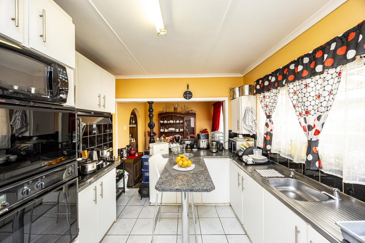 A functional kitchen featuring white cabinetry, granite countertops, a built-in oven and microwave, and ceramic tile flooring, with an open-plan layout to the dining area.