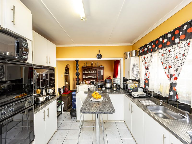 A functional kitchen featuring white cabinetry, granite countertops, a built-in oven and microwave, and ceramic tile flooring, with an open-plan layout to the dining area.