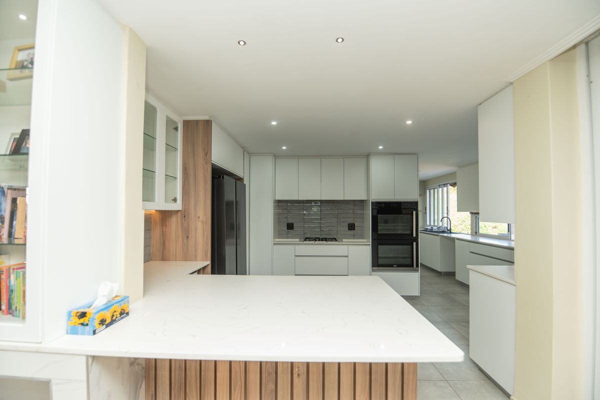 Modern, spacious kitchen featuring sleek white cabinetry, stone countertops, integrated double oven, gas hob, and a functional layout with ample storage.