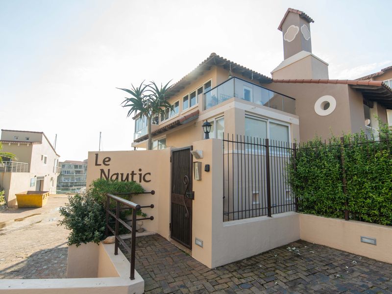 Front entrance view of Le Nautic apartment complex featuring a secure gated pedestrian access, paved driveway, and modern balcony balustrades.