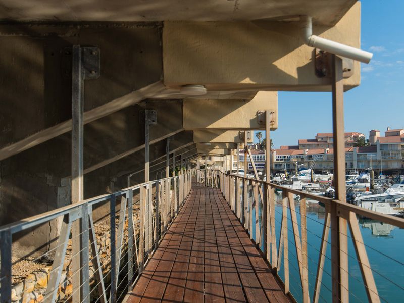 A wooden walkway balcony overlooking the marina, featuring metal balustrades and concrete structural supports.