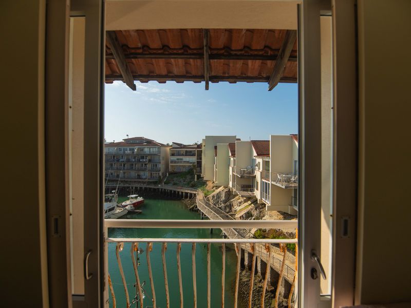 A view from an interior room looking out over a marina and surrounding apartment buildings, featuring a balcony with a metal railing.