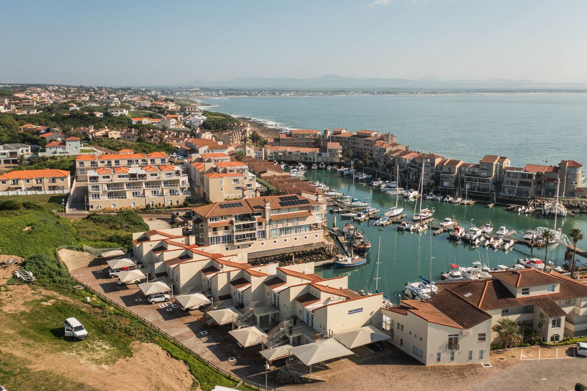 An aerial view of a coastal apartment complex featuring a private marina, tiled roofs, and dedicated carport parking areas.