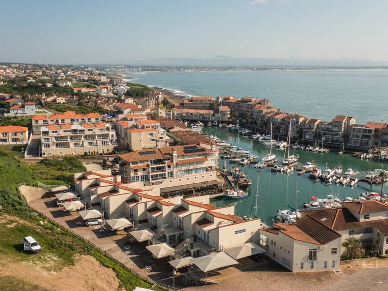 An aerial view of a coastal apartment complex featuring a private marina, tiled roofs, and dedicated carport parking areas.