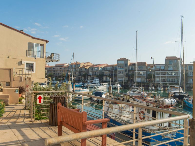 A scenic view overlooking a marina with docked boats and surrounding apartment buildings, featuring a paved walkway and metal safety railings.