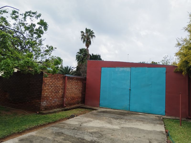 A detached garage featuring blue metal doors and a concrete driveway, set alongside a brick boundary wall in a garden setting.