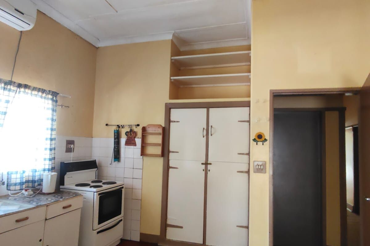 A dated kitchen featuring built-in cabinetry, a freestanding stove, and overhead shelving, showing signs of ceiling water damage and general wear.