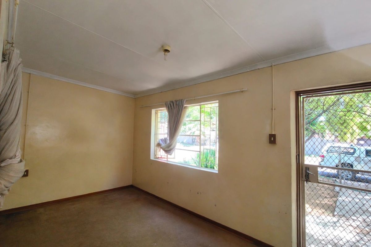 An empty living room featuring carpeted flooring, security bars on the windows, and a security gate at the entrance.