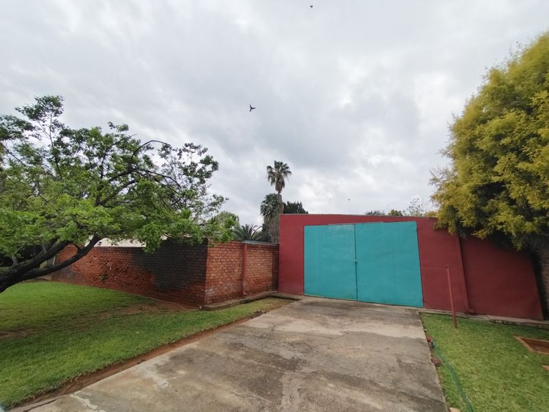 Rear exterior view featuring a concrete driveway, brick boundary wall, and a double garage with painted metal doors.