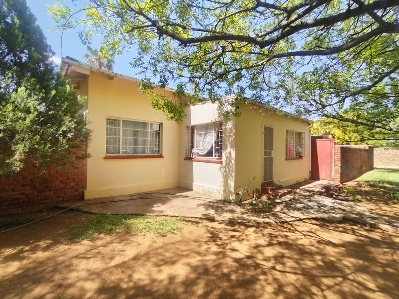 Rear view of the house featuring a concrete patio area, brick boundary walls, and security bars on the windows.