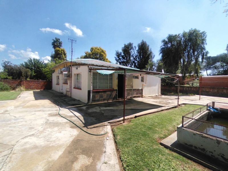 Rear view of the property featuring a concrete patio area, metal awning, and brick boundary walls, showing significant signs of wear and weathering.