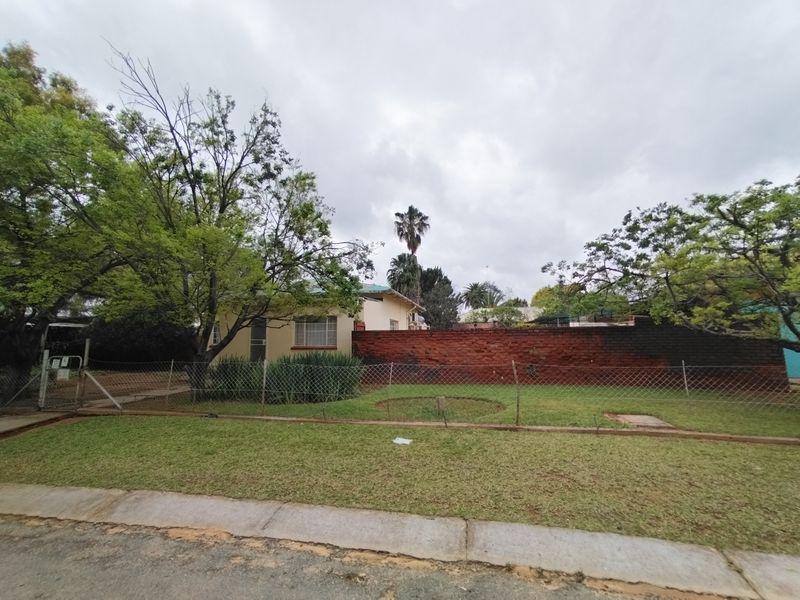 Front view of the property featuring a lawn, chain-link fencing, and a brick boundary wall.
