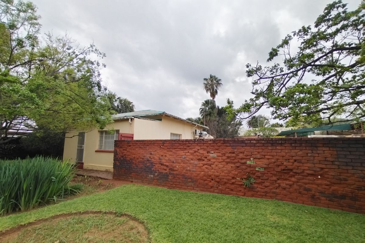 Rear view of the property featuring a lawn, a brick boundary wall, and the rear elevation of the house with a metal roof.