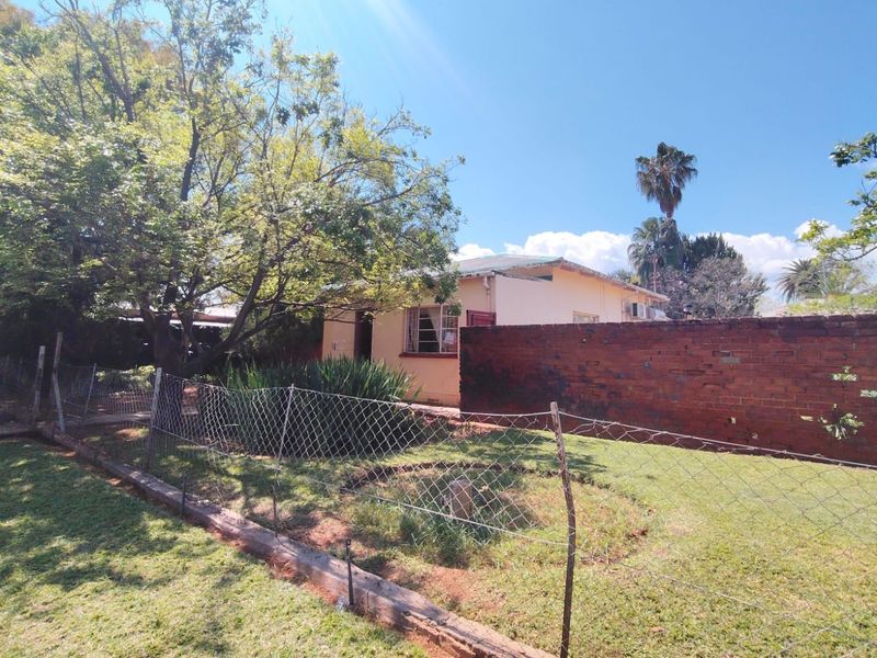 Rear exterior view of the property featuring a brick boundary wall, wire fencing, and established garden area with mature trees.