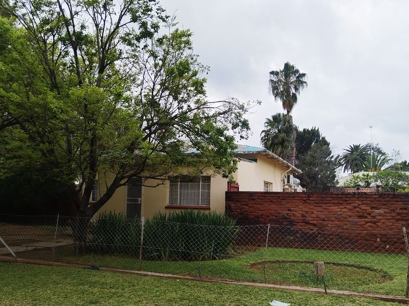 A view of the rear exterior of the house featuring a brick boundary wall, chain link fencing, and a mature garden setting.