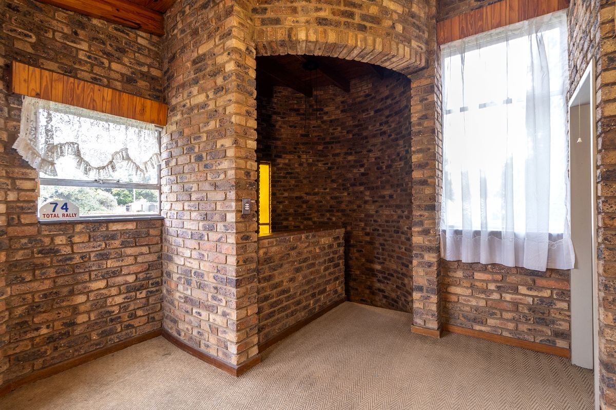 An empty living area featuring rustic exposed brick walls, a distinctive brick archway, and timber ceiling beams, offering a unique architectural character.