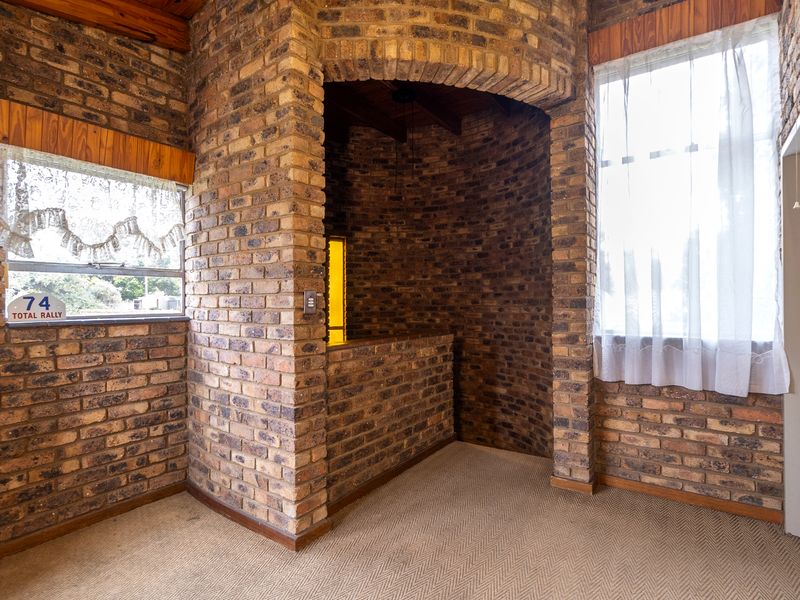 An empty living area featuring rustic exposed brick walls, a distinctive brick archway, and timber ceiling beams, offering a unique architectural character.
