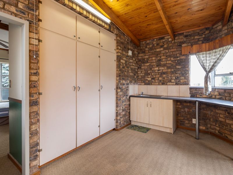 A functional scullery or utility area featuring exposed brick walls, timber ceiling beams, built-in storage cabinetry, and a sink with a countertop.