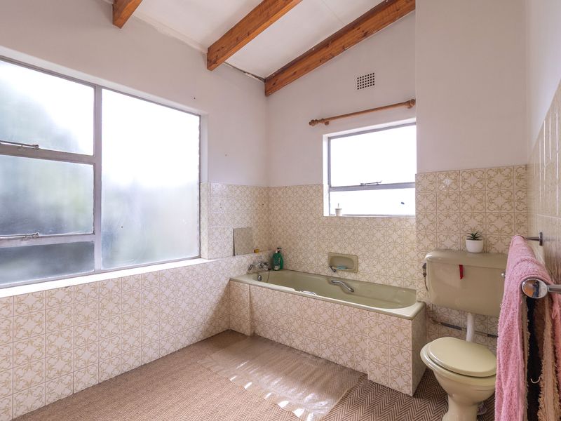 A dated bathroom featuring exposed timber ceiling beams, tiled walls, a built-in bathtub, and a standard toilet.