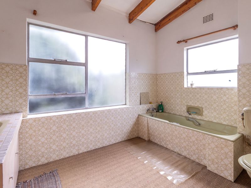 A spacious, dated bathroom featuring exposed timber ceiling beams, a built-in bathtub, and original tiled finishes, offering significant potential for a modern renovation.