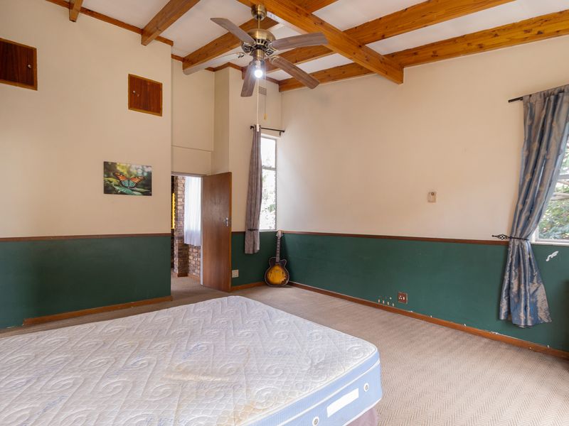 Bedroom featuring exposed timber ceiling beams, a ceiling fan, and wainscoting. The room offers a spacious layout with natural light and carpeted flooring.